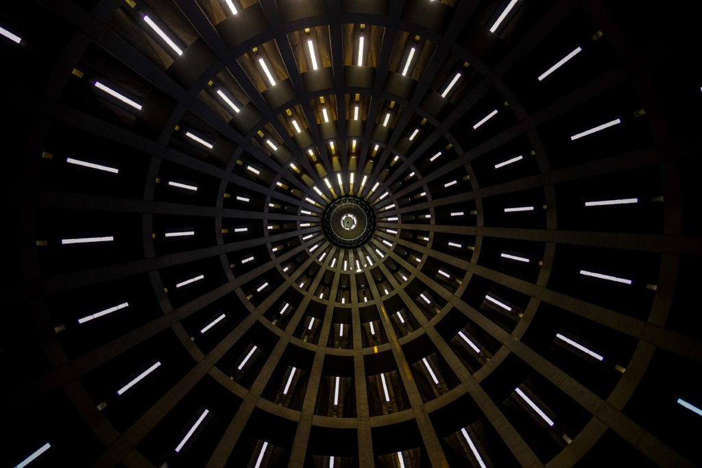 inside of a building looking up at the roof that is a dome shape wit light coming in from different open slots