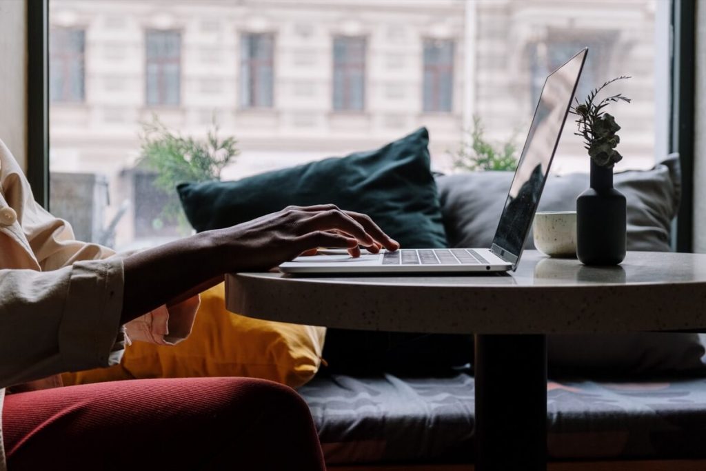 Person working on laptop on desk in front of a window.